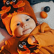 Lauren joined the competition — help win amazing prizes! baby, infant, orange_clothing, hat, bird_design, blanket, fruit, cute, cozy, smiling, indoor, child, portrait, warm_lighting, soft_texture, closeup, happy, headwear, playing, toddler