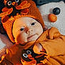 baby, infant, orange_clothing, hat, bird_design, blanket, fruit, cute, cozy, smiling, indoor, child, portrait, warm_lighting, soft_texture, closeup, happy, headwear, playing, toddler