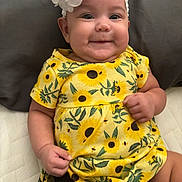 Jaelynn is registered to the contest to win money with this photo: baby, child, smile, happy, dress, yellow, sunflower, headband, flower, infant, cute, portrait, sitting, furniture, quilt, fabric, clothing, skin, person, indoors