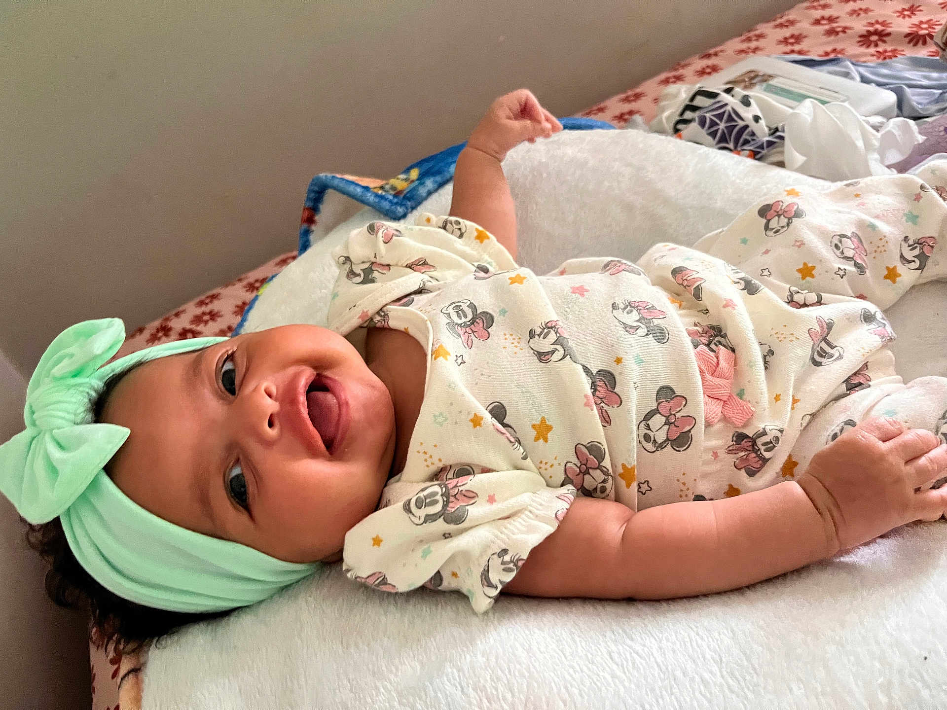 Areliana joined the competition — help win amazing prizes! baby, infant, smiling, headband, bow, onesie, minnie_mouse, patterned_clothing, blanket, bed, happy, cute, tongue_out, lying_down, soft_texture, indoor, child, person, playful, adorable