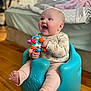 baby, baby_seat, bedroom, blanket, blue, cheerful, child, cute, floor, happy, home, indoor, infant, person, pink_clothing, playful, sitting, smiling, toy, wooden_floor
