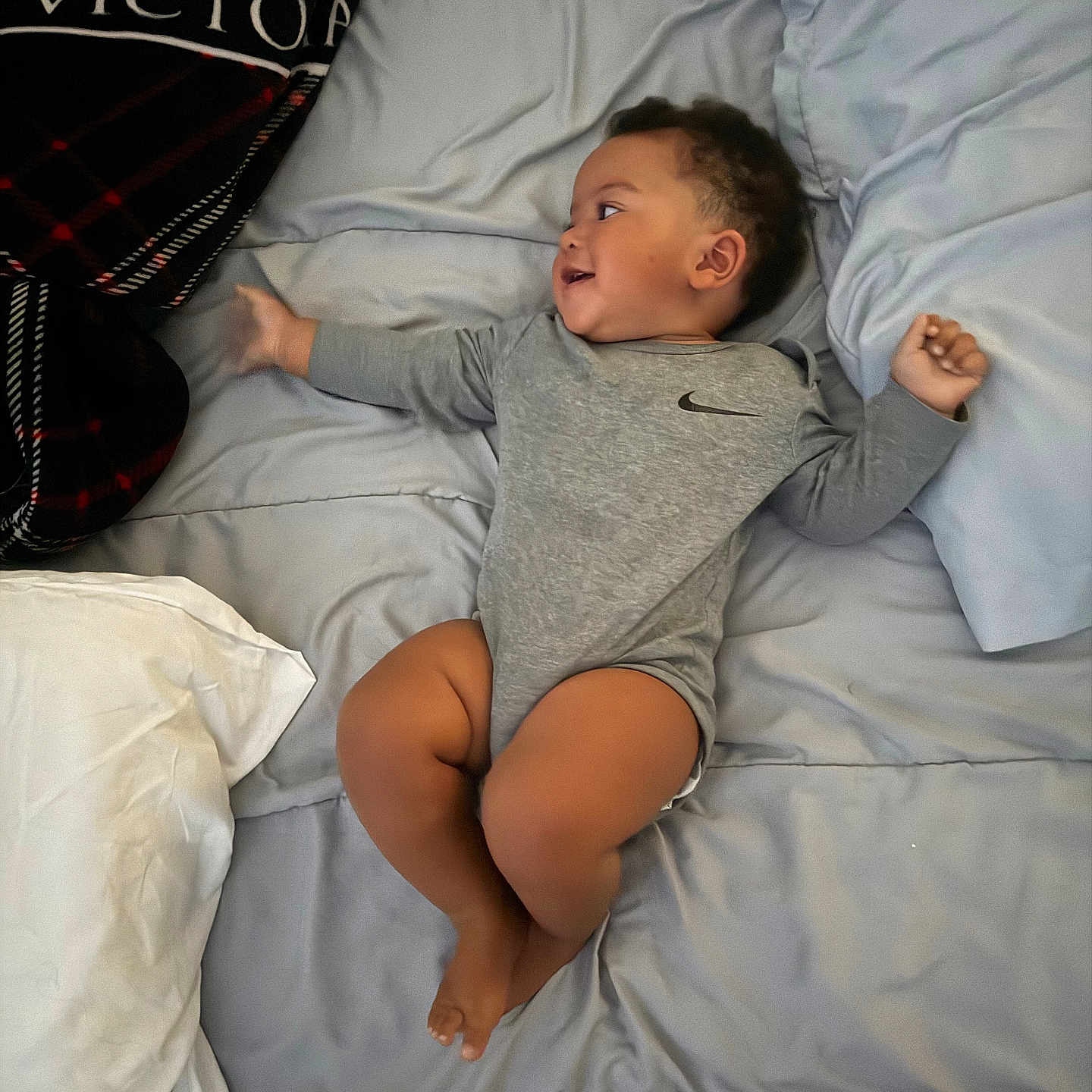 Quadir joined the competition — help win amazing prizes! baby, child, bed, pillow, blanket, onesie, nike, smile, lying_down, indoor, person, footwear, flip_flops, bedding, curly_hair, infant, happy, cute, relaxed, looking