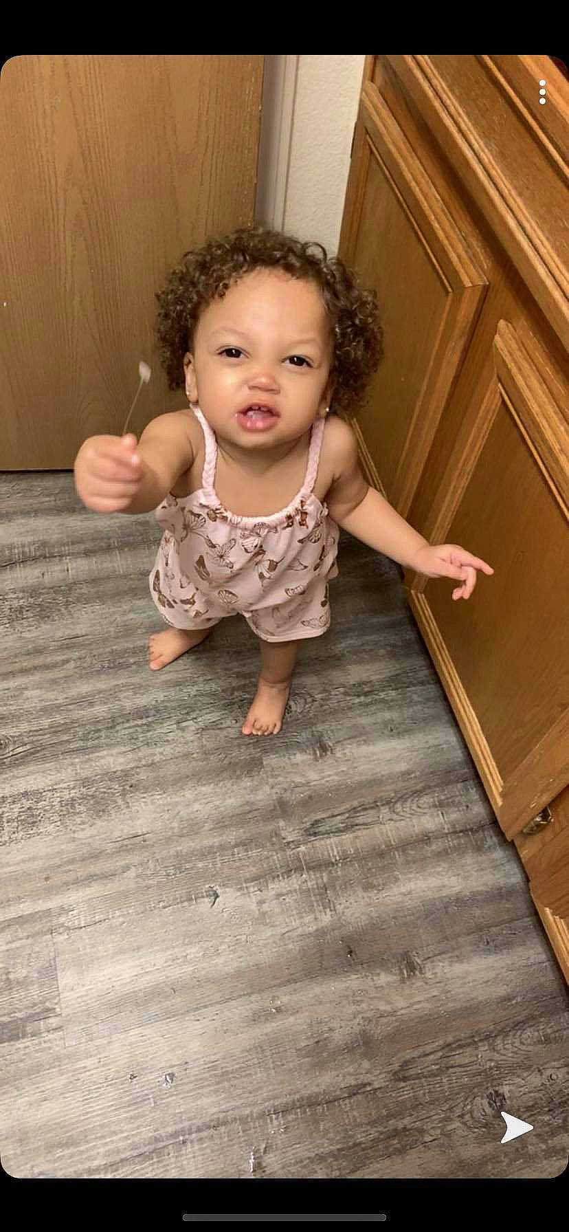 Ahmani is registered to the contest to win money with this photo: arm, baby, brown_hair, cheek, child, child_model, finger, floor, flooring, hardwood, laminate_flooring, leg, person, play, sitting, skin, standing, toddler, wood, wood_flooring