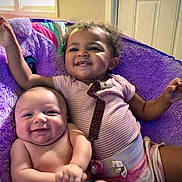 Amoni is registered to the contest to win money with this photo: baby, infant, child, smile, happy, cushion, purple, striped_shirt, diaper, pacifier_clip, indoors, window, door, furniture, curly_hair, skin, arm, hand, face, comfort