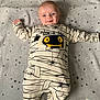 baby, infant, smile, onesie, clothing, blanket, stars, pattern, cute, happy, dimples, face, person, lying_down, child, spider, monster_design, text_on_clothing, indoors, soft_texture