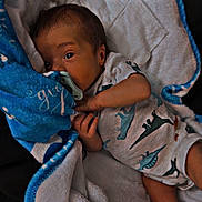 Giovanni joined the competition — help win amazing prizes! baby, blanket, child, cozy, cute, dinosaur_print, eyes, face, indoor, infant, lying_down, newborn, onesie, pacifier, resting, skin, sleepwear, small_hands, soft_texture, wrapped