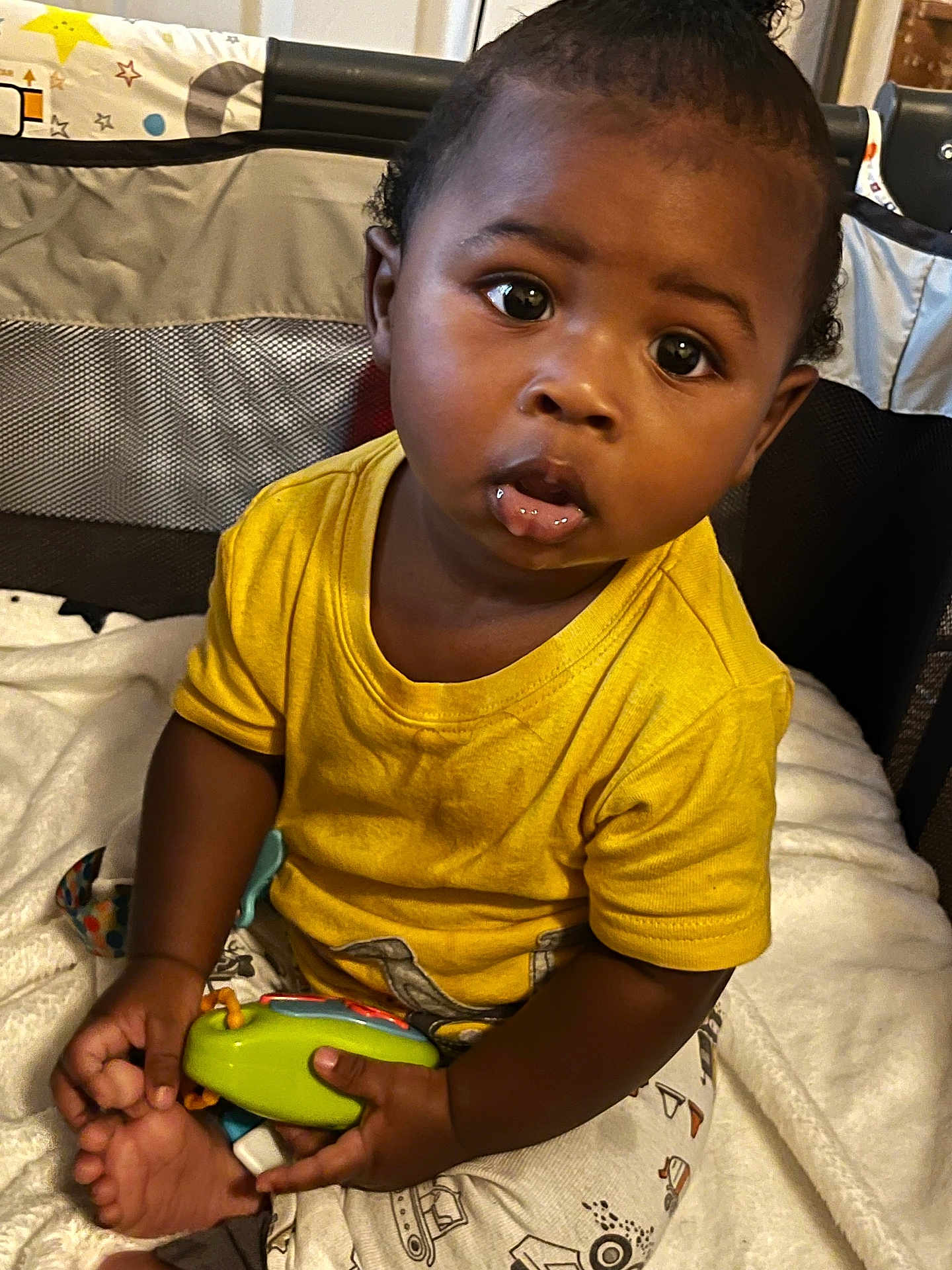 Kevion is registered to the contest to win money with this photo: baby, child, toy, yellow_shirt, blanket, playpen, curious, sitting, indoor, infant, cute, expression, hand, foot, clothing, person, portrait, young_child, bright_colors, soft_texture