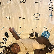 Kevion joined the competition — help win amazing prizes! baby, infant, smiling, hat, booties, onesie, lying_down, play_mat, numbers, star, happy, child, cute, indoors, floor, colorful, patterned, knitted, clothing, person