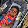 Kevion is registered to the contest to win money with this photo: baby, infant, car_seat, orange_clothing, striped, expression, scrunched_face, child, indoors, wooden_floor, seat, comfort, cute, person, portrait, hand, fingernails, head, hair, skin