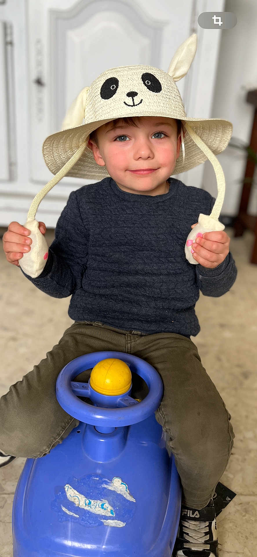 Maël a rejoint le concours — aidez-le/la à gagner de superbes lots ! child, hat, panda, toy_car, blue, yellow, sweater, indoor, floor, brown_pants, sneakers, smile, face, hands, play, cute, young_child, sitting, steering_wheel, fun