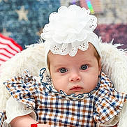 Samya joined the competition — help win amazing prizes! baby, infant, headband, flower, checked_dress, plaid, arm_bracelet, bracelet, fur_chair, patriotic_background, american_flag, stars, stripes, portrait, cute, child, young_baby, closeup, indoor, soft_lighting