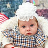 baby, infant, headband, flower, checked_dress, plaid, arm_bracelet, bracelet, fur_chair, patriotic_background, american_flag, stars, stripes, portrait, cute, child, young_baby, closeup, indoor, soft_lighting