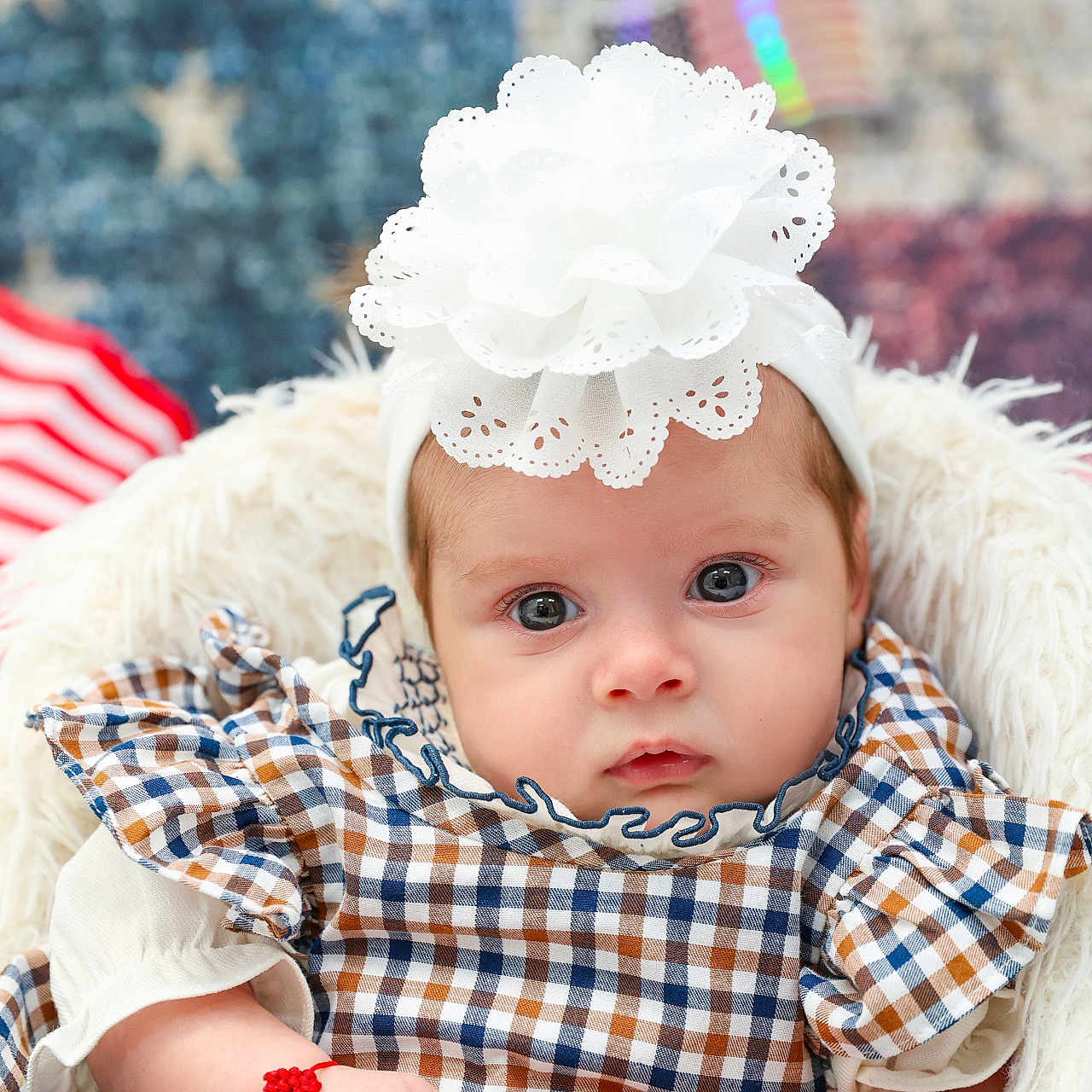 Samya joined the competition — help win amazing prizes! baby, infant, headband, flower, checked_dress, plaid, arm_bracelet, bracelet, fur_chair, patriotic_background, american_flag, stars, stripes, portrait, cute, child, young_baby, closeup, indoor, soft_lighting