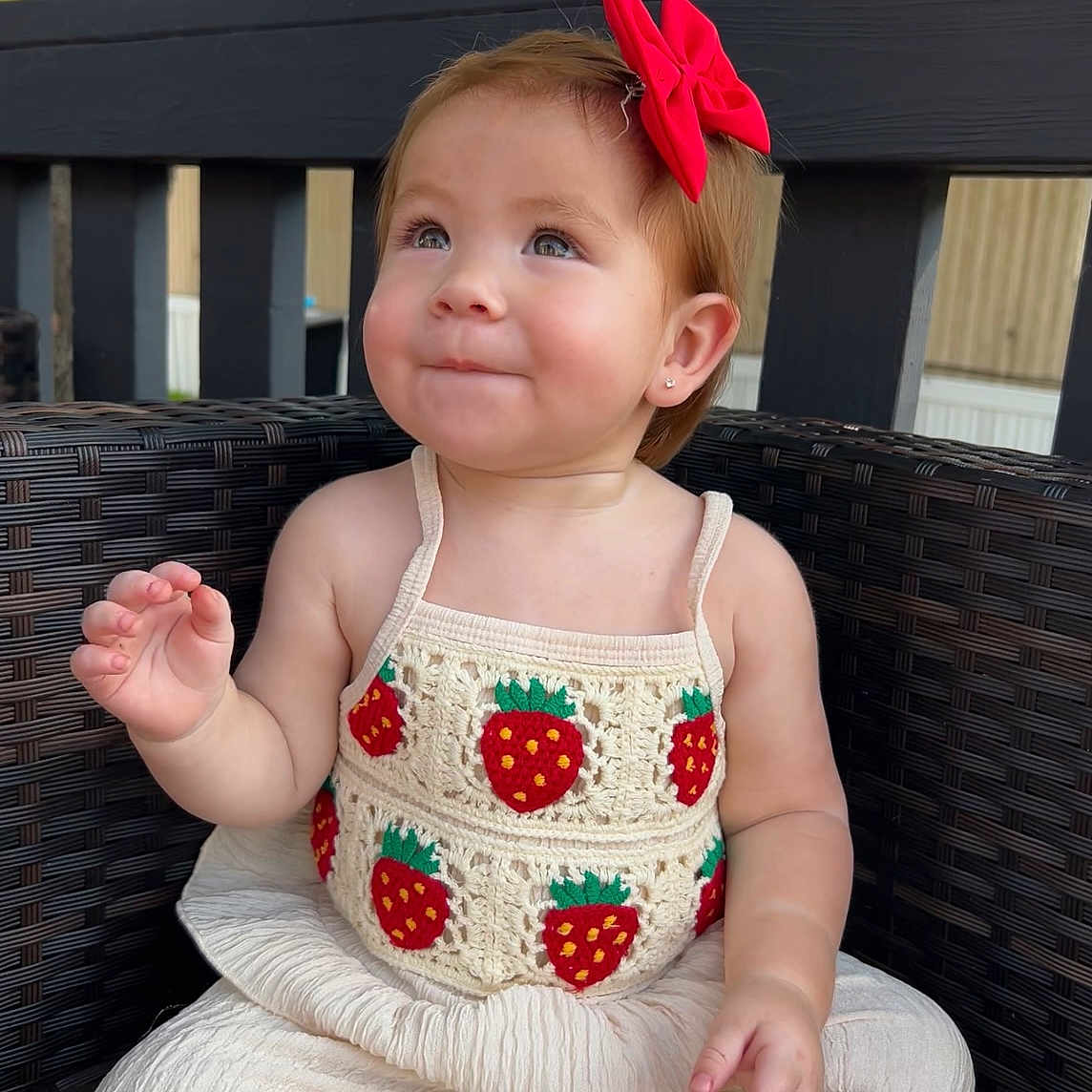 Jaylene is registered to the contest to win money with this photo: baby, casual_clothing, child, crochet_top, cute, earrings, happy, natural_light, outdoor, portrait, red_bow, short_hair, sitting, smile, strawberry_pattern, toddler, tree, white_pants, wicker_chair, wooden_fence