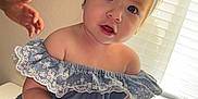 Jaylene is registered to the contest to win money with this photo: baby, blinds, blue_clothing, bow, child, curious, cute, face, hand, headband, indoor, infant, light, off_shoulder, portrait, remote_control, sitting, skin, table, window
