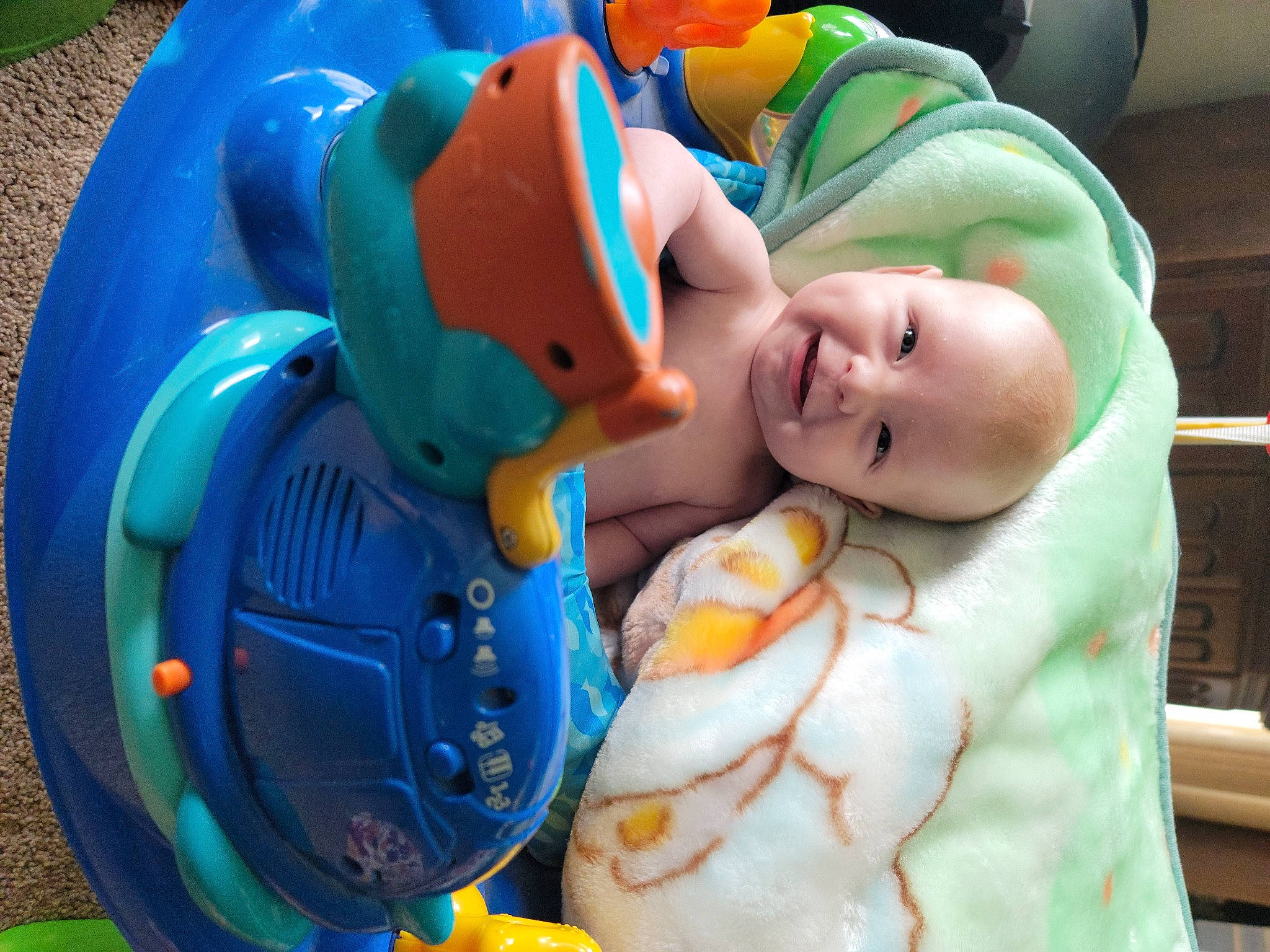 James is registered to the contest to win money with this photo: baby, baby_products, baby_safety, baby_toddler_clothing, baby_toys, child, comfort, electric_blue, fun, green, happy, joy, mouth, person, personal_protective_equipment, plastic, room, smile, stuffed_toy, toddler