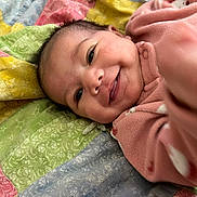 Romy joined the competition — help win amazing prizes! apparel, baby, blanket, child, closeup, colorful, cute, expression, face, happy, indoor, infant, lying_down, pink_clothing, portrait, quilt, reaching_hand, skin, smile, young