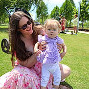 Ruby is registered to the contest to win money with this photo: baby, woman, child, grass, outdoor, park, stroller, sunglasses, purple_clothing, white_pants, smile, sunny, trees, people, casual, daylight, happy, nature, kneeling, holding