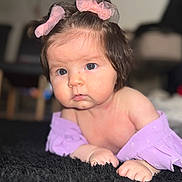 Emmy is registered to the contest to win money with this photo: baby, child, infant, face, eyes, hair, bows, purple_clothing, carpet, floor, skin, cute, portrait, indoor, person, young_child, lying_down, expression, soft_texture, curious