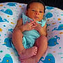 baby, infant, pillow, whale_pattern, blue_blanket, clothing, face, hands, feet, indoors, person, cute, newborn, resting, young_child, soft_texture, sleeping_area, baby_garment, expression, tiny_fingers