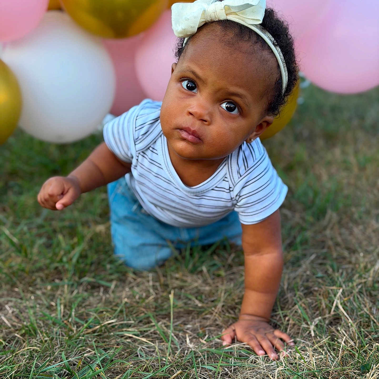 Jestinne is registered to the contest to win money with this photo: toddler, child, baby, crawling, grass, balloons, headband, white_bow, outdoor, nature, curious, young_child, striped_shirt, blue_pants, portrait, cute, innocence, expression, celebration, playful