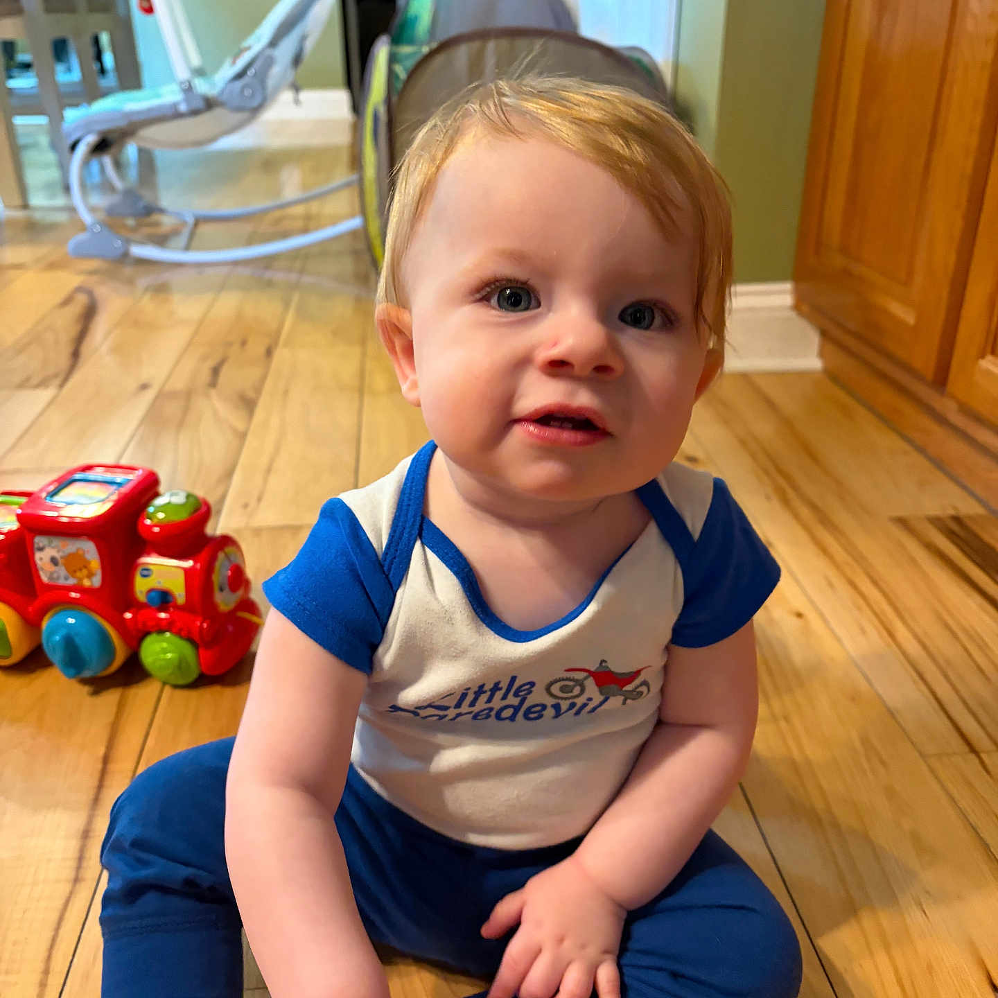 Lincoln is registered to the contest to win money with this photo: toddler, child, baby, floor, toy, red_train, blue_clothing, wooden_floor, indoor, home, cabinets, curious, sitting, playtime, cute, smiling, person, young_child, hands, face