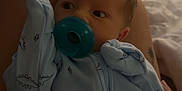 Lincoln joined the competition — help win amazing prizes! baby, pacifier, blue_onesie, dinosaur_pattern, infant, person, lap, home_interior, blanket, furniture, soft_lighting, sleepwear, newborn, couch, relaxing, cute, child, indoors, comfort, resting