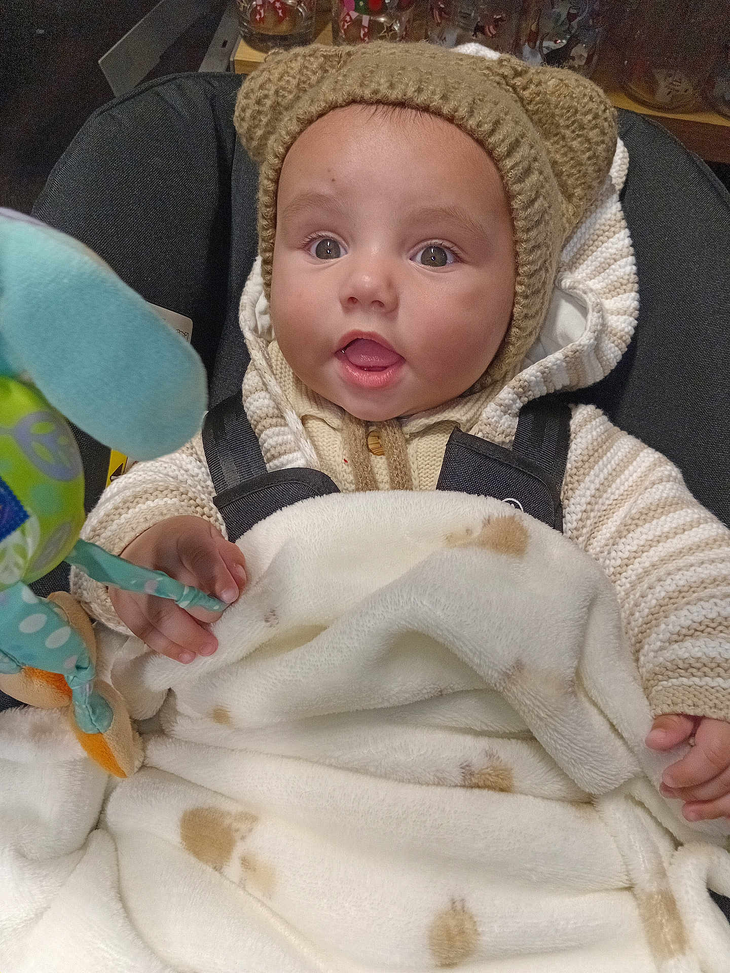 Theo joined the competition — help win amazing prizes! baby, infant, child, knitted_hat, bear_ears, blanket, soft_toy, car_seat, warm_clothing, striped_sweater, cute, curious, indoors, portrait, face, hands, expression, cozy, wrapped, seated