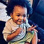Luca is registered to the contest to win money with this photo: toddler, child, smiling, curly_hair, indoor, bed, clothing, shorts, long_sleeve_shirt, person, skin, face, happy, playing, sitting, expression, cute, young, baby, casual
