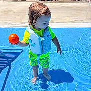 Kolton is registered to the contest to win money with this photo: toddler, child, pool, water, life_jacket, orange_ball, swimwear, sunny_day, shadow, outdoor, people, lounge_chairs, swimming_pool, summer, recreation, play, fun, water_play, vacation, park
