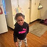 child, birthday_crown, hoodie, puma, upset, barefoot, wooden_floor, indoor, rug, cleaning_tools, sweatshirt, person, expression, home, curly_hair, pants, standing, face, emotion, casual_clothing