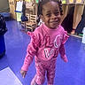child, pink_clothing, smiling, indoor, classroom, floor, shoes, hair, furniture, educational_materials, cabinet, chair, person, walking, happy, young, playful, colorful, school, portrait