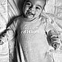 baby, infant, smiling, onesie, blanket, black_and_white, portrait, happy, lying_down, cute, face, child, clothing, text_on_clothing, soft_texture, cozy, indoors, young_child, expression, sleepwear