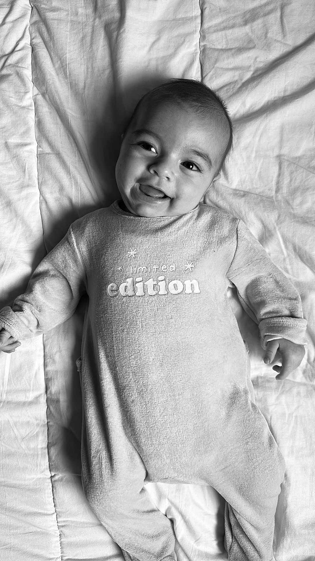 Lucas a rejoint le concours — aidez-le/la à gagner de superbes lots ! baby, infant, smiling, onesie, blanket, black_and_white, portrait, happy, lying_down, cute, face, child, clothing, text_on_clothing, soft_texture, cozy, indoors, young_child, expression, sleepwear