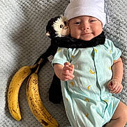 Kavion joined the competition — help win amazing prizes! baby, infant, plush_toy, monkey_toy, banana, onesie, hat, blanket, smiling, cute, lying_down, soft_toy, baby_clothing, cozy, indoor, child, happy, toy, fruit, portrait
