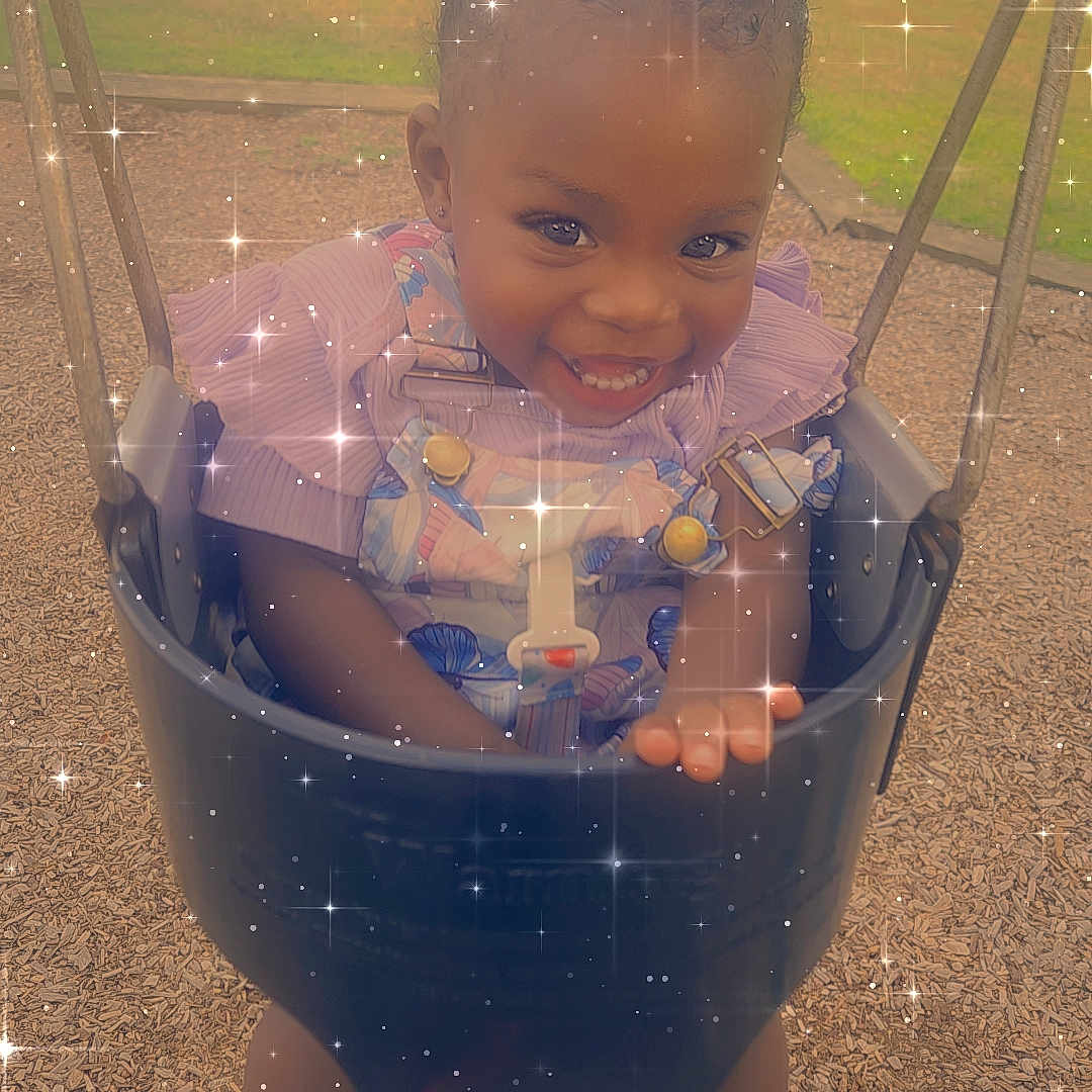 Samiera is registered to the contest to win money with this photo: child, curly_hair, cute, daylight, dress, fun, grass, happy, joyful, outdoor, park, play_equipment, playground, safety_harness, shoes, smiling, sparkle_effect, swing, toddler, wood_chips
