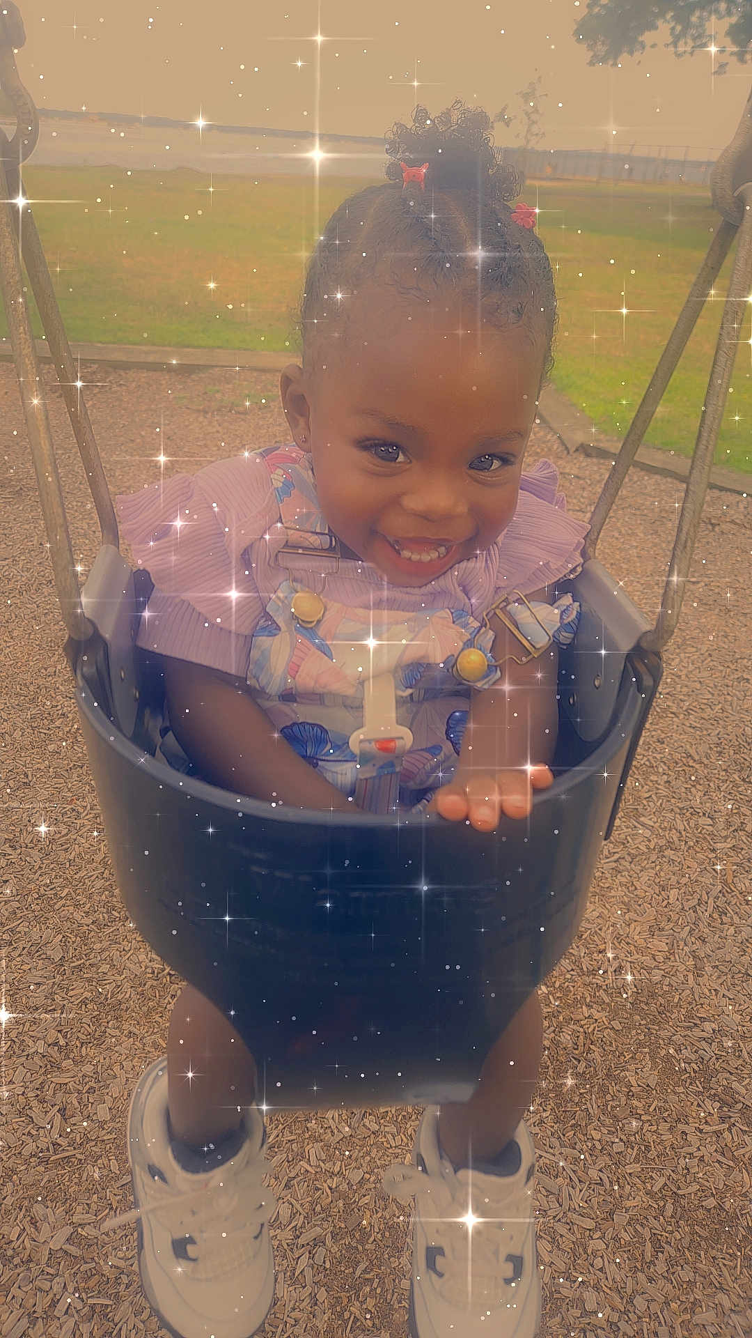 Samiera is registered to the contest to win money with this photo: toddler, child, swing, playground, smiling, happy, outdoor, shoes, curly_hair, dress, safety_harness, wood_chips, grass, play_equipment, joyful, cute, daylight, park, sparkle_effect, fun