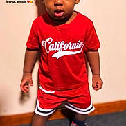 Demari is registered to the contest to win money with this photo: child, toddler, boy, portrait, standing, smiling, red_shirt, red_shorts, knit_cap, sneakers, sportswear, indoor, wall, carpet, fashion, full_body, looking_at_camera, text_overlay, casual_clothing, playful