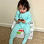 toddler, child, pajamas, blue_pajamas, polka_dot, indoor, floor, cardboard_box, bread, snack, sitting, curious_expression, wall, tile_floor, person, young_child, clothing, face, hair, pacifier_clip