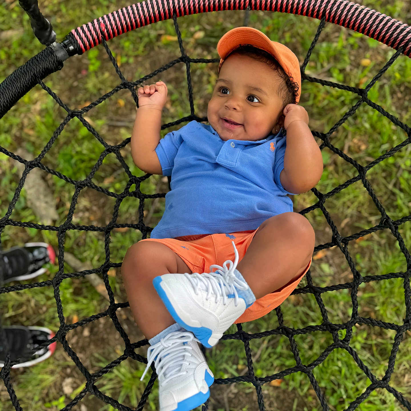Traesyn is registered to the contest to win money with this photo: baby, blue_shirt, casual, child, cute, feet, footwear, grass, happy, leisure, net_swing, orange_cap, orange_shorts, outdoor, person, play, smiling, summer, swing, white_sneakers