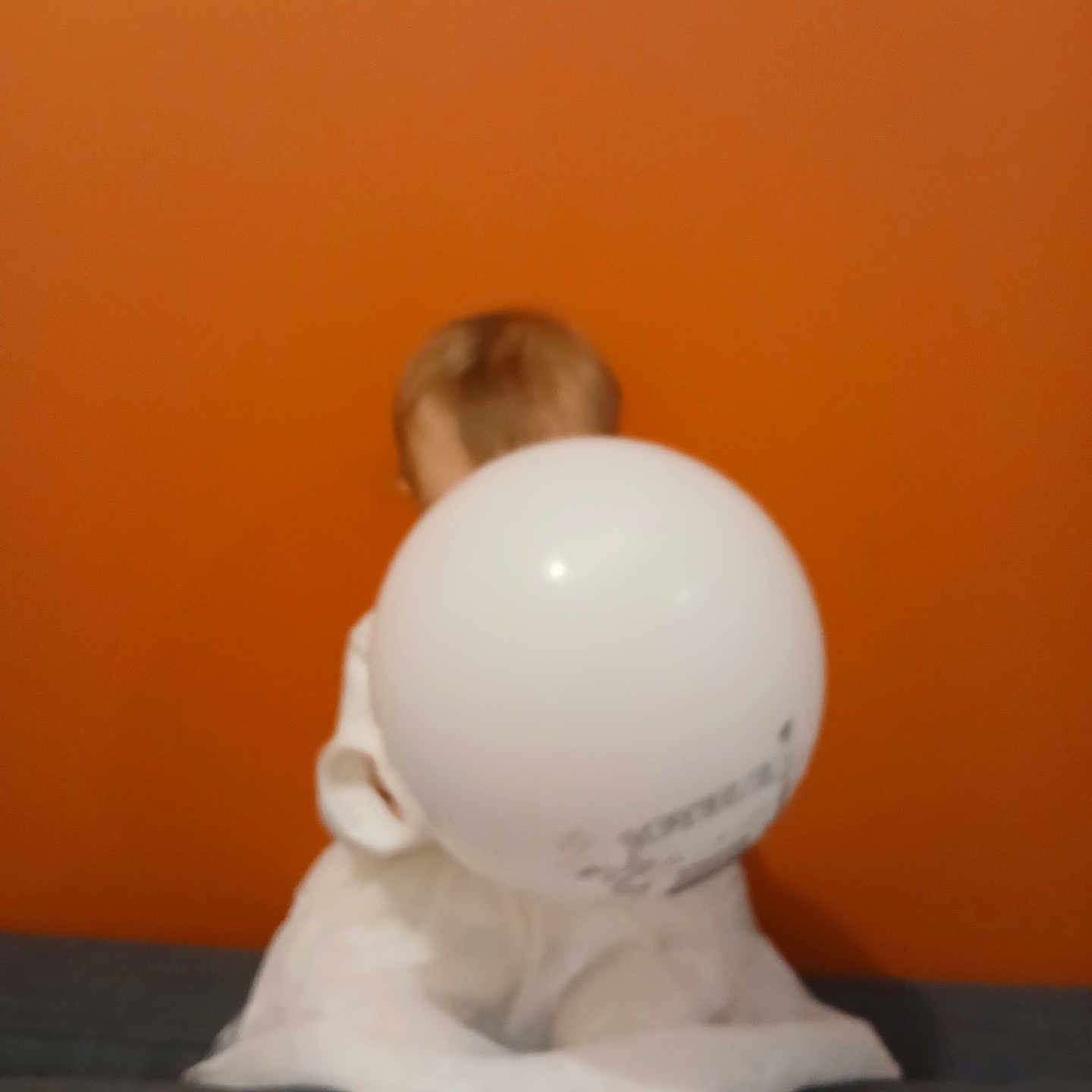 Mon Coeur participe au concours pour gagner de l'argent avec cette photo : background, balloon, blurry, casual, child, couch, furniture, head, holding, home, indoor, legs, orange_wall, person, room, sitting, soft_toys, toy, unfocused, white_clothing