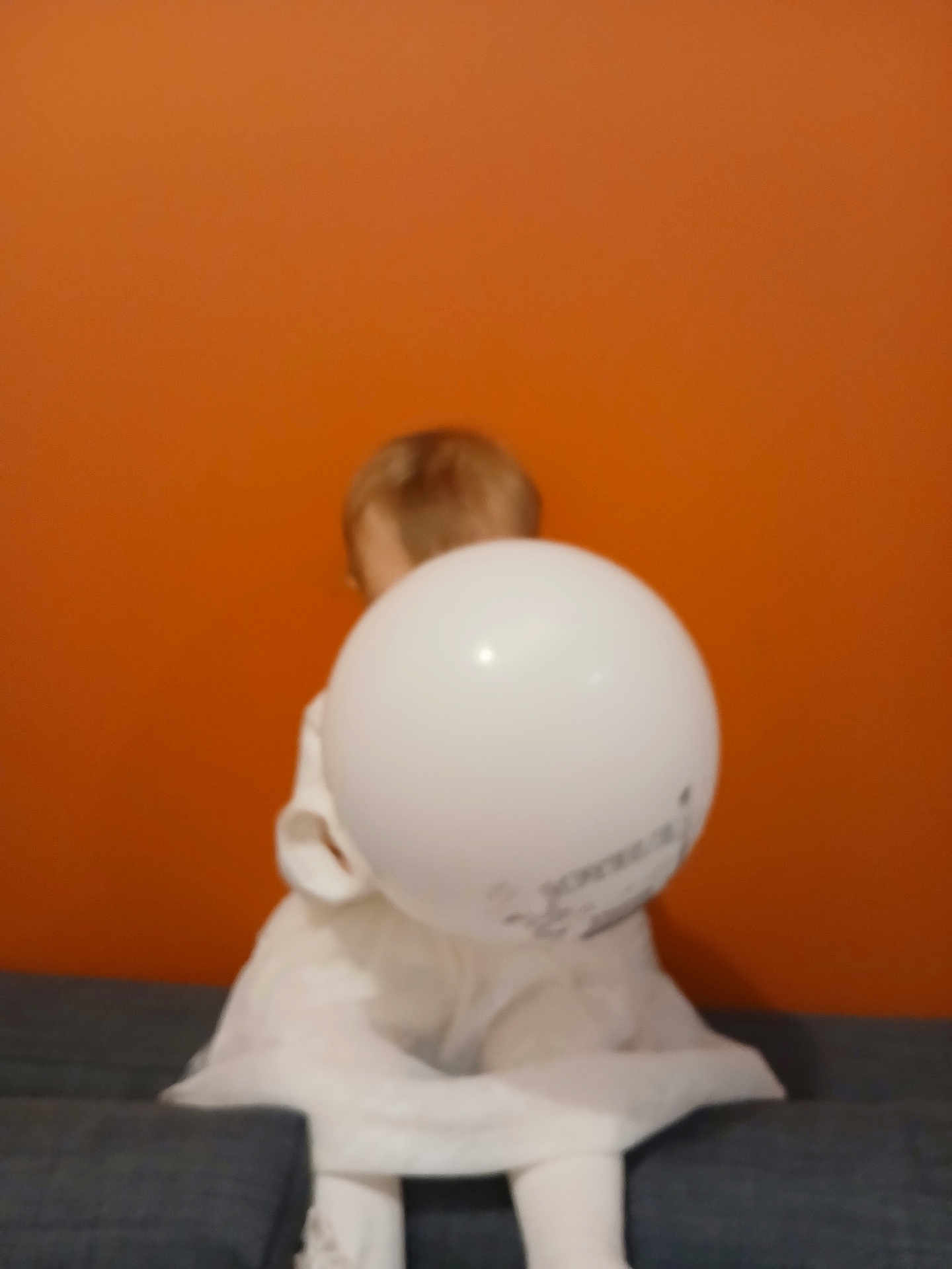 Mon Coeur participe au concours pour gagner de l'argent avec cette photo : background, balloon, blurry, casual, child, couch, furniture, head, holding, home, indoor, legs, orange_wall, person, room, sitting, soft_toys, toy, unfocused, white_clothing