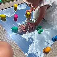 Paisley is registered to the contest to win money with this photo: toddler, mirror, reflection, sky, clouds, grass, plastic_eggs, child, smile, outdoor, play, colorful, toy, sunlight, happy, face, reflection_art, nature, spring, cute