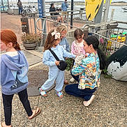 Atlas is registered to the contest to win money with this photo: children, woman, cat, outdoor, waterfront, boats, surfboard, casual_clothing, sidewalk, railing, flower_pot, people, daylight, interaction, petting, smiling, summer, hair_bow, jeans, hoodie