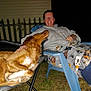 Denver is registered to the contest to win money with this photo: person, dog, outdoor, night, chair, smile, pet, grass, fence, casual_clothing, blanket, relaxation, animal, friendship, companion, happy, leisure, comfort, paw, headrest