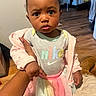 Malasianay joined the competition — help win amazing prizes! baby, infant, child, portrait, sitting, indoors, bedroom, tutu, pink_jacket, nike_shirt, bow, curly_hair, dark_skin, serious_expression, looking_at_camera, adult_hand, wood_floor, bed, clothing, fashion