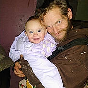 Patience is registered to the contest to win money with this photo: baby, child, man, beard, jacket, indoor, smile, happy, person, clothing, face, holding, purple_jacket, facial_hair, expression, portrait, human, warm_clothing, light, background