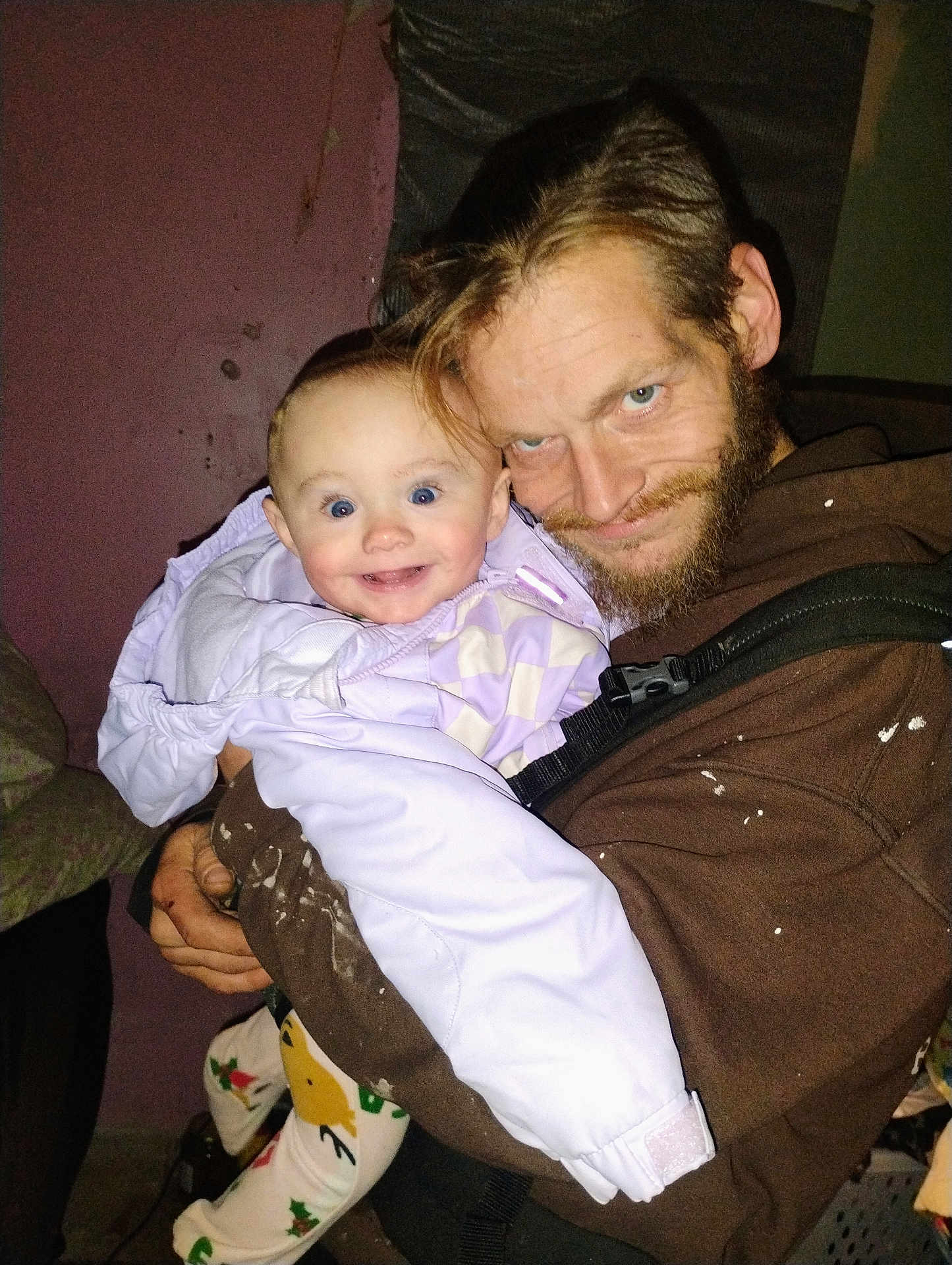 Patience is registered to the contest to win money with this photo: baby, child, man, beard, jacket, indoor, smile, happy, person, clothing, face, holding, purple_jacket, facial_hair, expression, portrait, human, warm_clothing, light, background