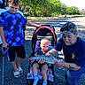 baby, blue_shirt, boy, cap, casual_clothing, child, family, fish, gravel, man, nature, outdoor, recreation, road, sandals, smile, socks, stroller, sunlight, trees