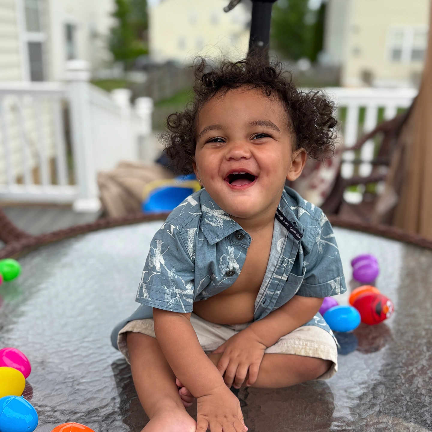 Diquan joined the competition — help win amazing prizes! baby, barefoot, child, curly_hair, daylight, fun, glass_table, happy, house, outdoor, person, plastic_eggs, playful, porch, railing, shirt, shorts, sitting, smiling, toddler